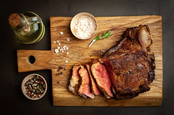Siyah taş arka plan üzerinde ahşap doğrama tahtası üzerinde baharat ile Yağlı ızgara domuz biftek