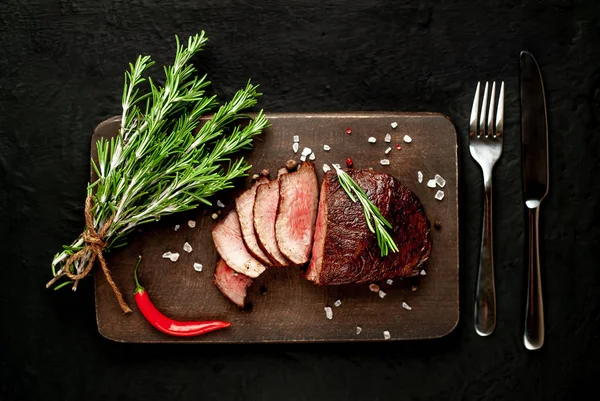 Siyah taş arka plan üzerinde baharat ve biberiye dalları ile Taze ızgara biftek