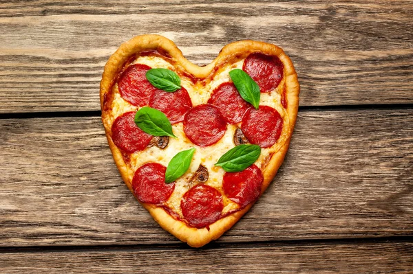 ahşap arka plan üzerinde salam ve taze fesleğen yaprakları ile peynir kalp pizza