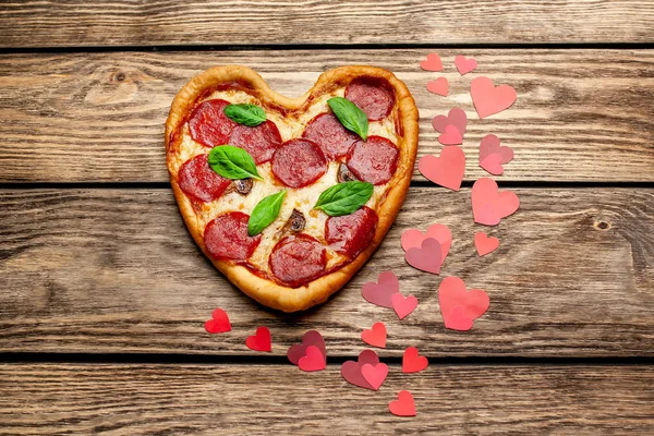 cheese heart pizza with salami and fresh basil leaves on wooden background with heart shape red confetti