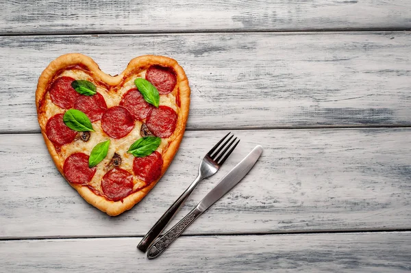 ahşap arka plan üzerinde salam ve taze fesleğen yaprakları ile peynir kalp pizza