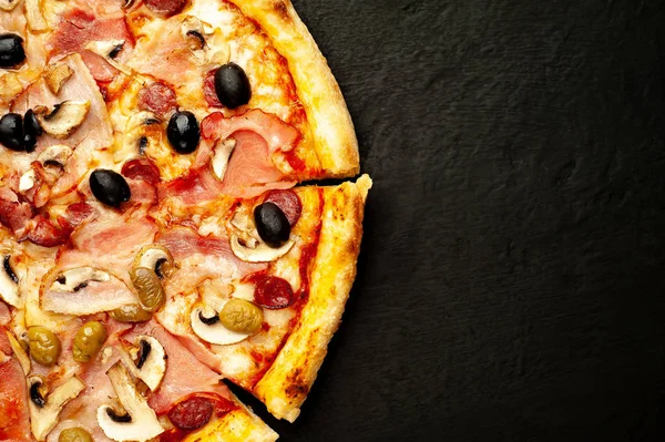 Siyah taş arka plan üzerinde mantar, domates, zeytin ve jambon ile taze ev yapımı pizza