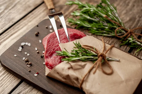 Ahşap doğrama tahtası üzerinde biberiye dalları ile zanaat kağıt sarılmış çiğ sığır eti biftek