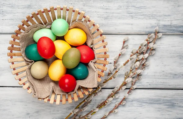 Beyaz ahşap arka planda renkli Paskalya yumurtaları ve kedi söğüt dalları ile sepet