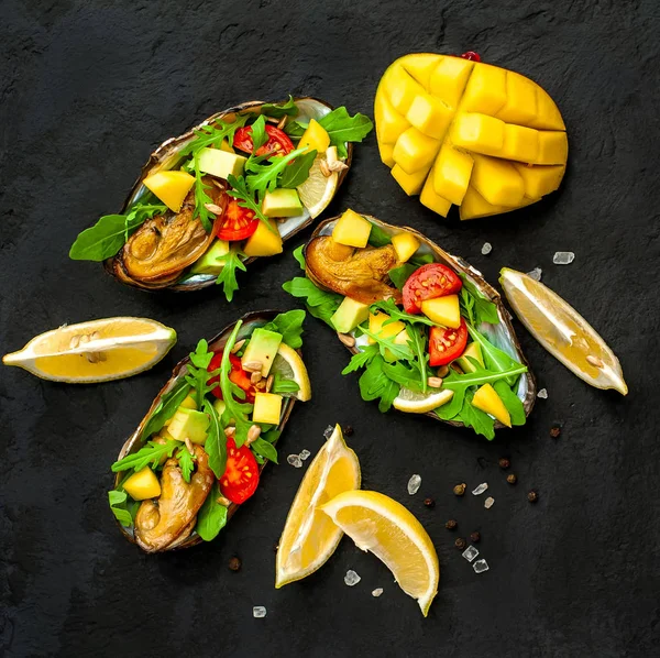 Siyah beton arka plan üzerinde avokado, arugula, mango, domates ve limon dilimleri ile pişmiş midye