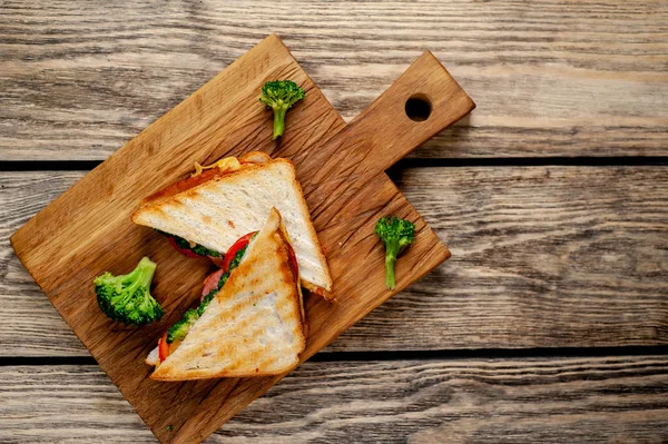 Ahşap doğrama tahtasında jambon, taze brokoli ve peynirile taze ızgara sandviçler