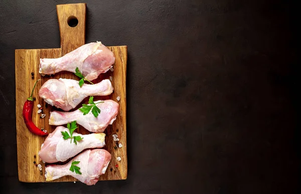 Chicken legs with spices, chili pepper and parsley leaves on wooden chopping board