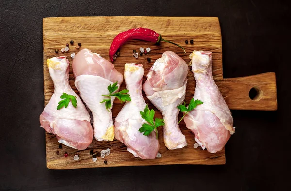 Chicken legs with spices,salt, chili pepper and parsley leaves on wooden board over black stone background