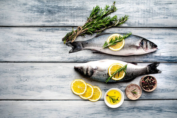 Raw fish with lemon slices and rosemary twigs on grey wooden background
