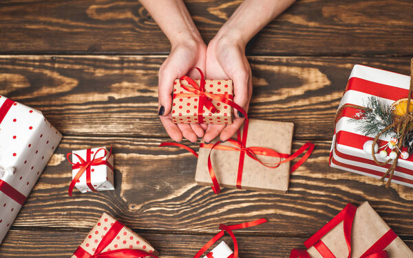 Female hands decorating gift boxes with red bows on old wooden background 