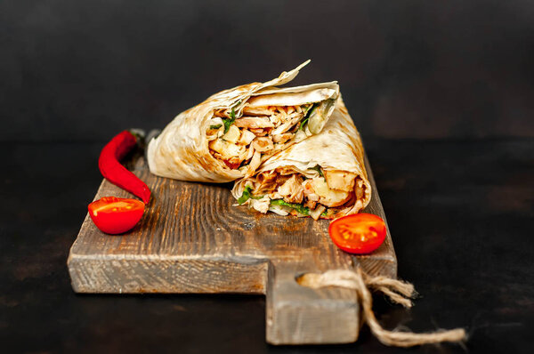 Traditional mexican burrito wrapped with chicken and vegetables served with ripe tomatoes on wooden chopping board 