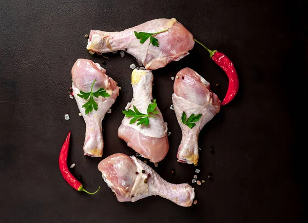 Chicken legs with spices, chili pepper and parsley leaves on black stone background
