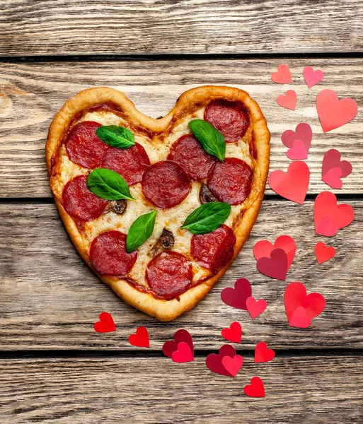 cheese heart pizza with salami and fresh basil leaves on wooden background with heart shape red confetti