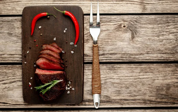 Ahşap arka planda baharat ve biberiye dalları ile taze ızgara biftek