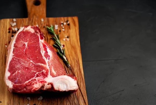Taş arka plan üzerinde ahşap doğrama tahtası üzerinde baharat ve biberiye dal ile Çiğ yağlı biftek