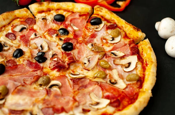 Fresh homemade pizza with mushrooms, tomatoes, olives and ham on black stone background