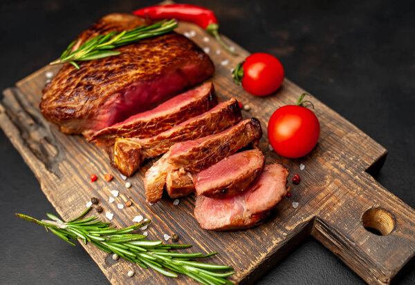 Fresh juicy medium rare beef steak served with chili pepper and rosemary twigs on wooden board