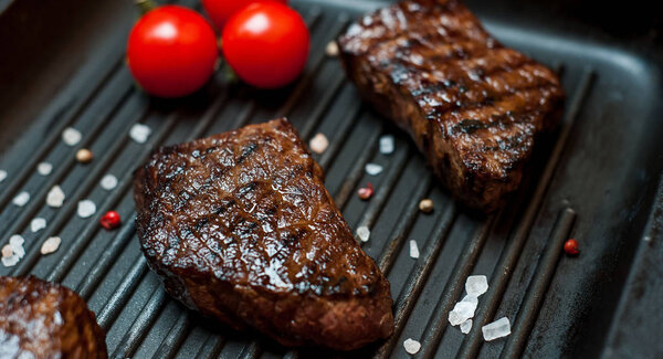 Fresh grilled steaks on grill pan with fresh tomatoes
