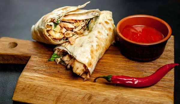 Traditional mexican burrito wrapped with chicken and vegetables with spicy sauce on wooden chopping board