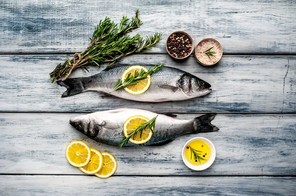Gri ahşap arka plan üzerinde limon dilimleri ve biberiye dalları ile çiğ balık