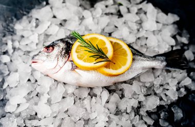 Soğuk ezilmiş buz yığını üzerinde limon dilimleri ve biberiye ile taze balık yakın görünümü