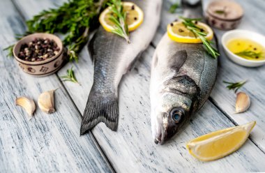 Gri ahşap arka plan üzerinde limon dilimleri ve biberiye dalları ile çiğ balık