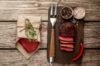 Dilimlenmiş biftek ve çiğ biftek ahşap arka plan üzerinde zanaat kağıt sarılmış