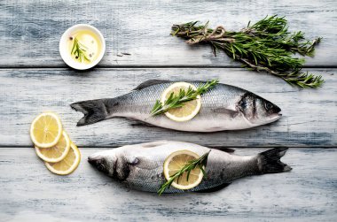 Gri ahşap arka plan üzerinde limon dilimleri ve biberiye dalları ile çiğ balık