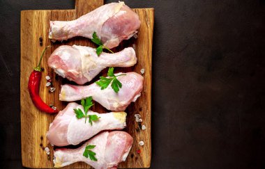 Ahşap doğrama tahtası üzerinde baharat, biber ve maydanoz yaprakları ile Tavuk bacakları 