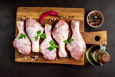 Siyah taş arka plan üzerinde ahşap doğrama tahtası üzerinde baharat, tuz, maydanoz yaprakları ve yağ şişesi ile Tavuk bacakları