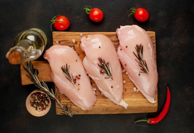 Ahşap doğrama tahtasında tuz, biberiye dalları ve zeytinyağı şişesi ile çiğ tavuk fileto