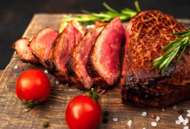 Ahşap doğrama tahtası üzerinde biberiye dalları ile dilimlenmiş orta nadir sığır eti biftek yakın görünümü