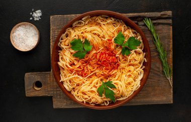 koyu taş arka plan üzerinde domates sosu ve maydanoz yaprakları ile İtalyan spagetti makarna