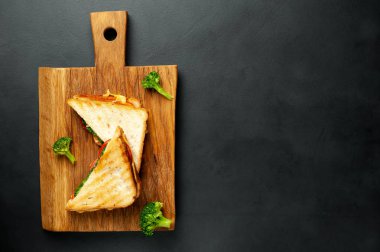 Ahşap doğrama tahtasında jambon, taze brokoli ve peynirile taze ızgara sandviçler