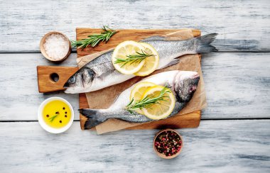 Ahşap doğrama tahtası üzerinde limon dilimleri ve biberiye dalları ile çiğ balık