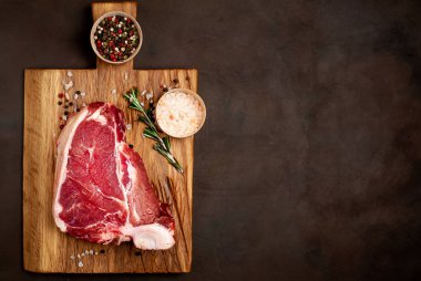 Taş arka plan üzerinde ahşap doğrama tahtası üzerinde baharat ve biberiye dal ile Çiğ yağlı biftek