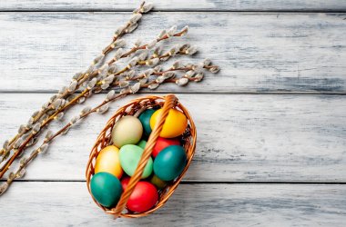 Beyaz ahşap arka planda renkli Paskalya yumurtaları ve kedi söğüt dalları ile sepet