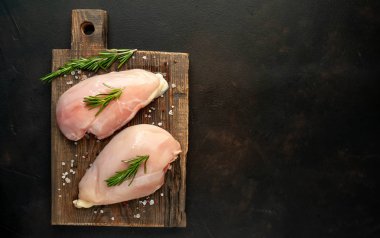 Ahşap doğrama tahtası üzerinde tuz ve biberiye dalları ile Çiğ tavuk fileto