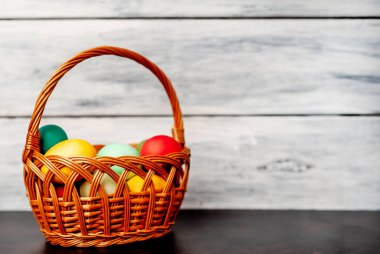 Beyaz ahşap arka plan üzerinde renkli Paskalya ile sepet yumurta