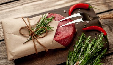 Ahşap doğrama tahtası üzerinde biberiye dalları ile zanaat kağıt sarılmış çiğ sığır eti biftek