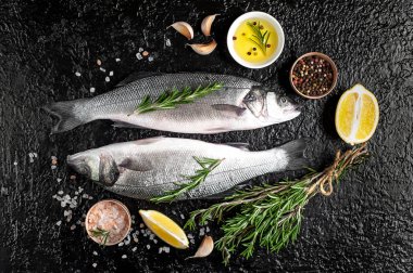 Siyah taş arka plan üzerinde limon, baharat ve biberiye dalları ile çiğ balık