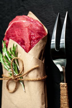 Çiğ sığır eti biftek taş arka plan üzerinde biberiye dalları ile zanaat kağıt sarılmış 
