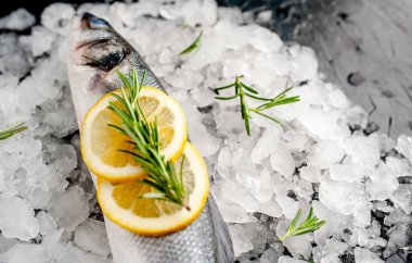 Soğuk ezilmiş buz yığını üzerinde limon dilimleri ve biberiye ile taze balık yakın görünümü