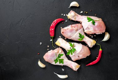 Baharat, biber ve maydanoz yaprakları ile tavuk bacakları siyah taş arka plan üzerinde