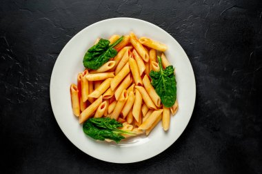 taş siyah arka plan üzerinde yeşil yaprakları ile servis domates soslu makarna