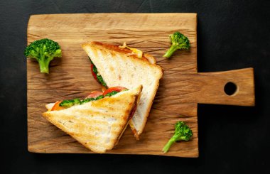 Ahşap doğrama tahtasında jambon, taze brokoli ve peynirile taze ızgara sandviçler