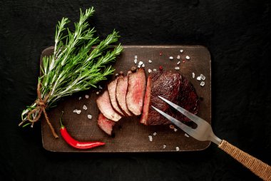 Siyah taş arka plan üzerinde baharat ve biberiye dalları ile Taze ızgara biftek