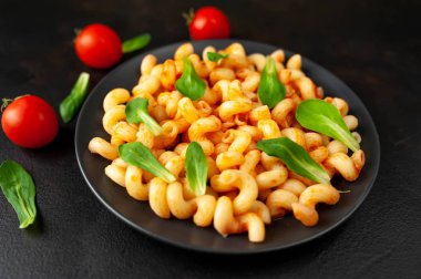 domates soslu makarna, yeşil yapraklar ve taş siyah arka plan üzerinde olgun domates