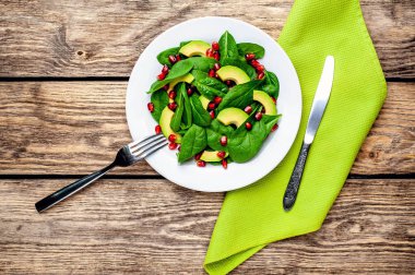 Ahşap masada ıspanak yaprakları, avokado dilimleri ve nar taneleri ile taze yeşil salata 