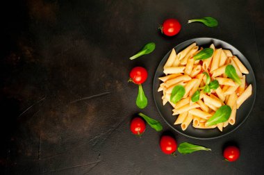 domates soslu makarna, yeşil yapraklar ve taş siyah arka plan üzerinde olgun domates